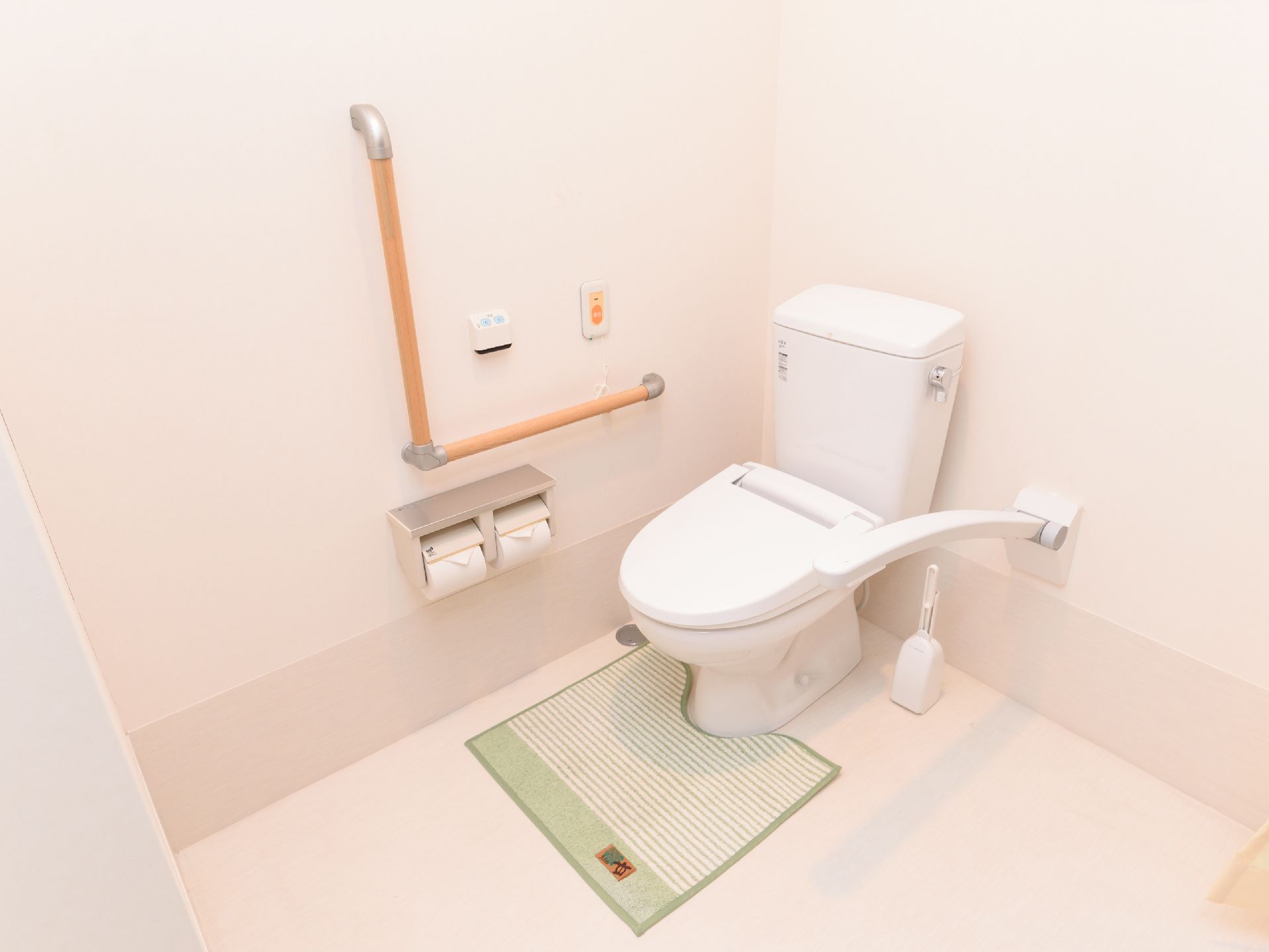 トイレは広いスペースに設置されている。可動式のひじ掛けがあり、便座脇の壁には縦横つながった手すりがついている。