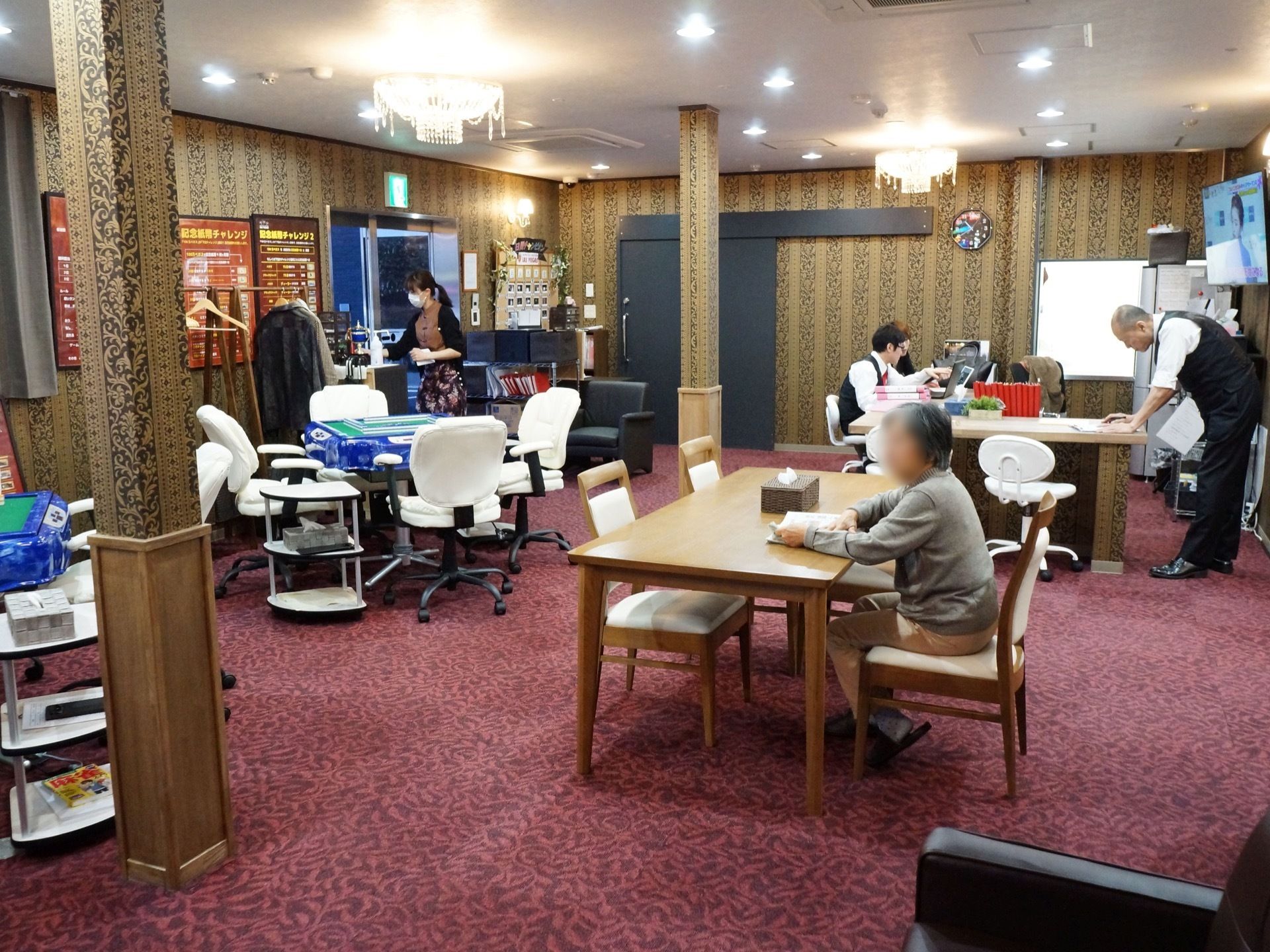 部屋には麻雀台が置かれている。近くには茶色いテーブルが置かれ、席には入居者様が座っている。スタッフも数人いる。