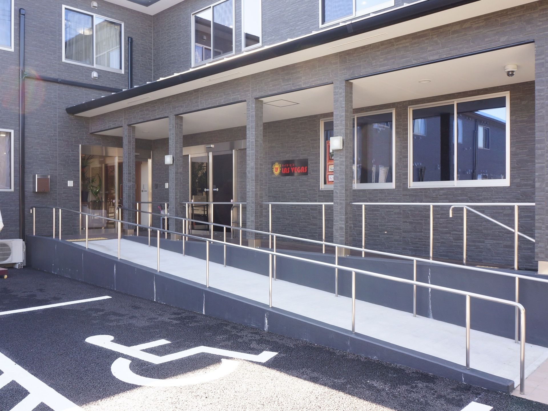施設敷地内には車椅子専用駐車場がある。すぐ近くは施設の入口になっており、手すりが付けられたスロープがある。