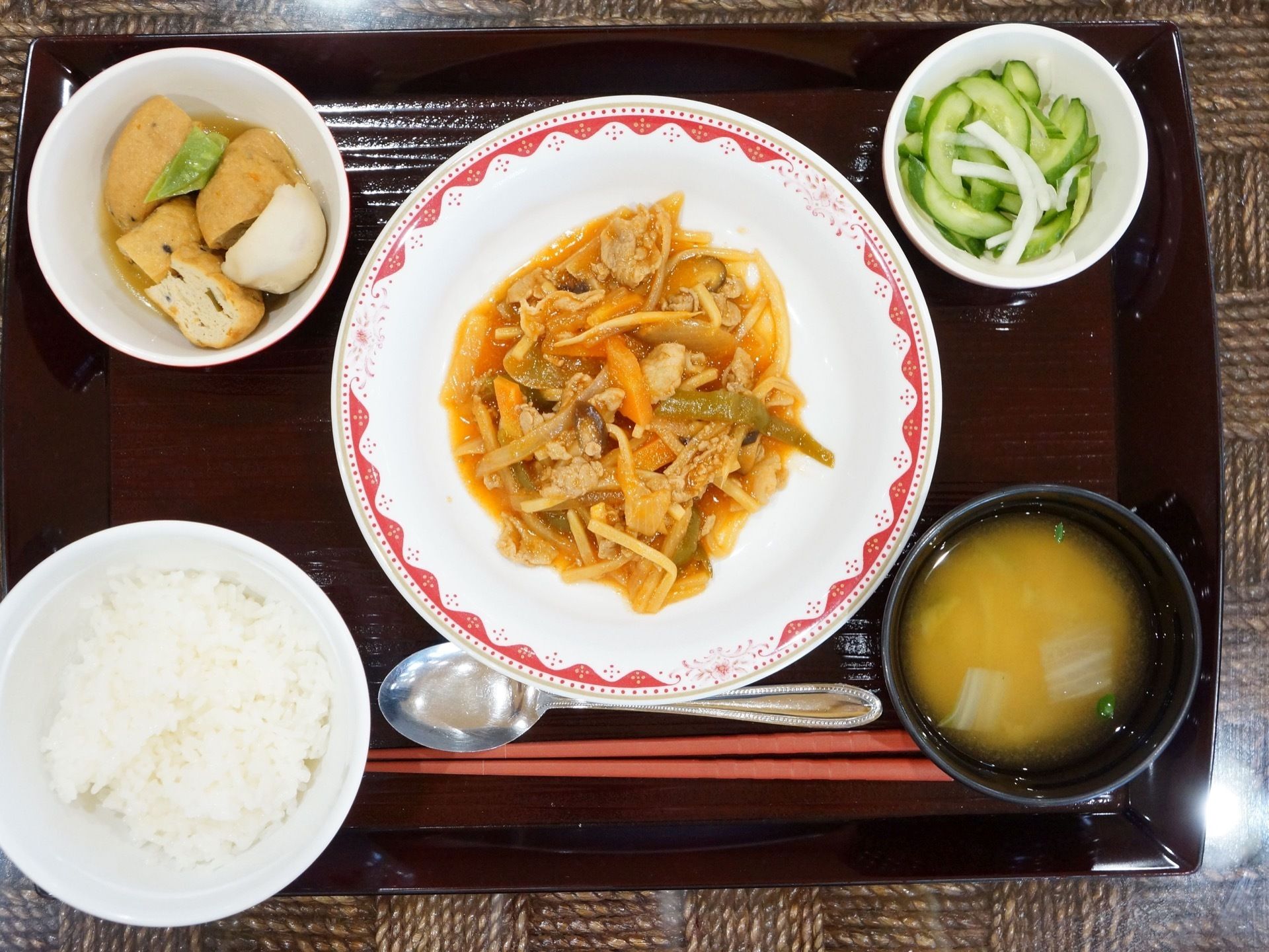 黒いお盆の上にご飯やお味噌汁、キュウリのお漬物、がんもの煮つけなどが乗っている。野菜が多くヘルシーなメニューである。
