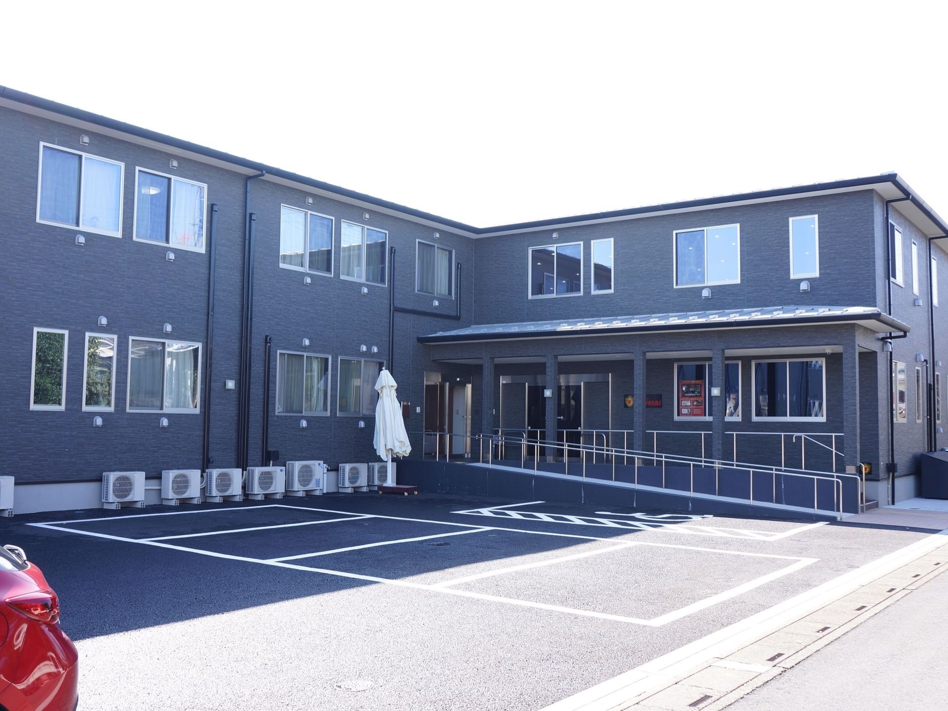 2階建ての施設の外観は黒色である。入口には緩やかなスロープが設置されている。スロープがある横は車の駐車スペースになっている。