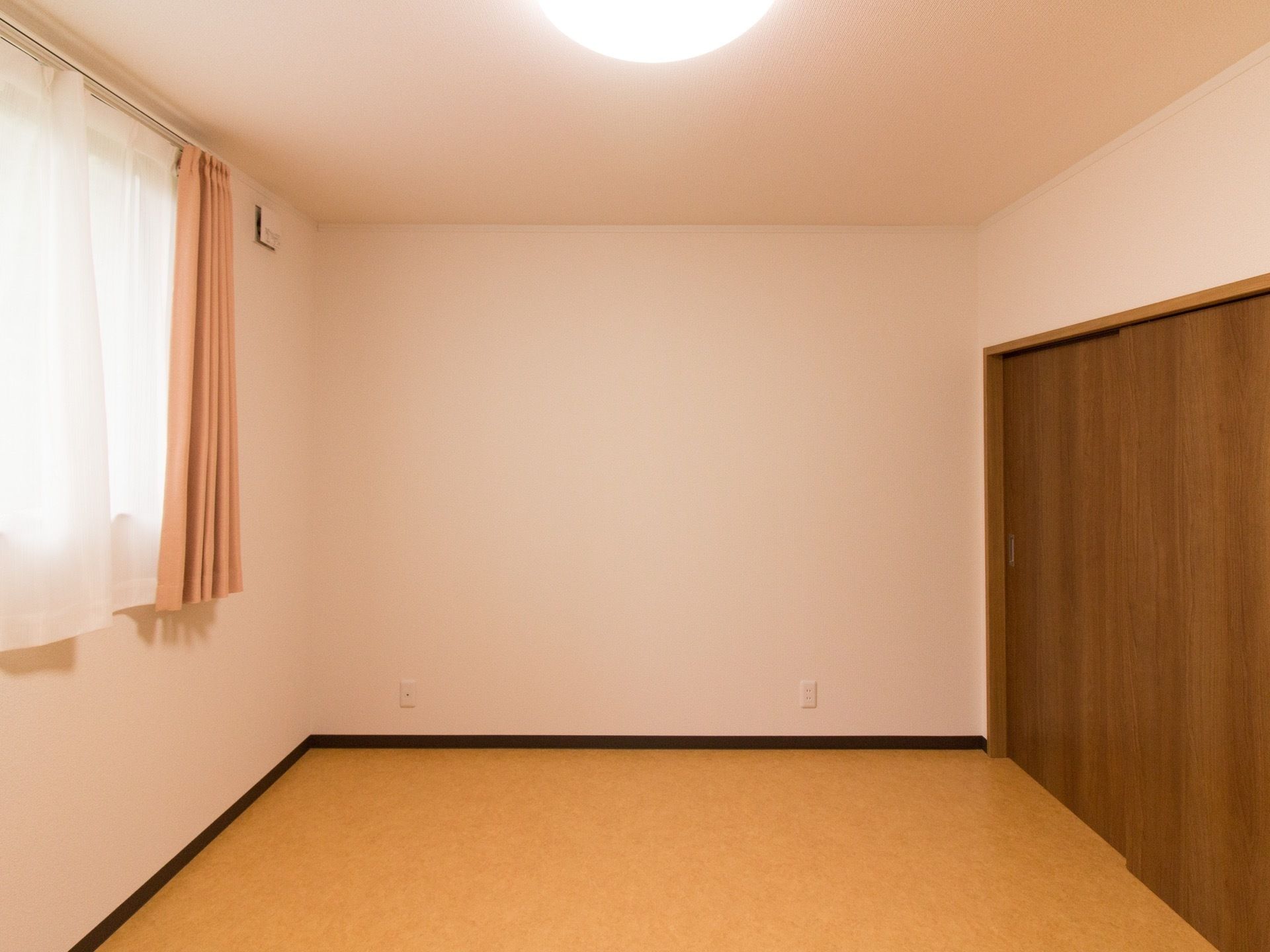 あたたかみのある色合いの居室である。収納スペースが広くとられており、大きな窓もある。ベッドを置いても十分スペースに余裕がある。