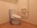 木目調の床、白い壁の洋式トイレである。温水洗浄便座を完備。壁には緊急呼び出しボタンが設置されている。