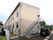 ツートンカラーの2階建ての建物で、側面に外階段がある。隣の建物との間には白いフェンスが設置されている。
