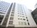 マンションのような外観の白い壁には、数多くの窓が設置されている。左側にあるグレーの柵の向こうには、室外機が置かれている。