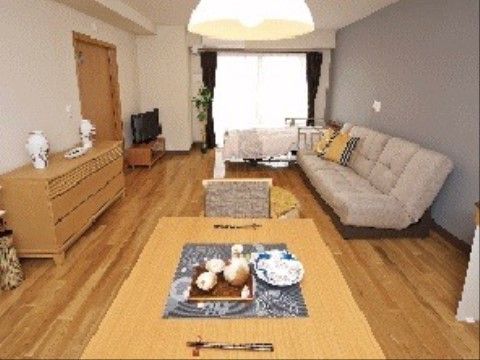 広々とした室内には、ベッド、ソファ、テレビ、タンス、テーブルと椅子のほか観葉植物が置かれ、広いガラス引き戸とカーテンが設置されている。