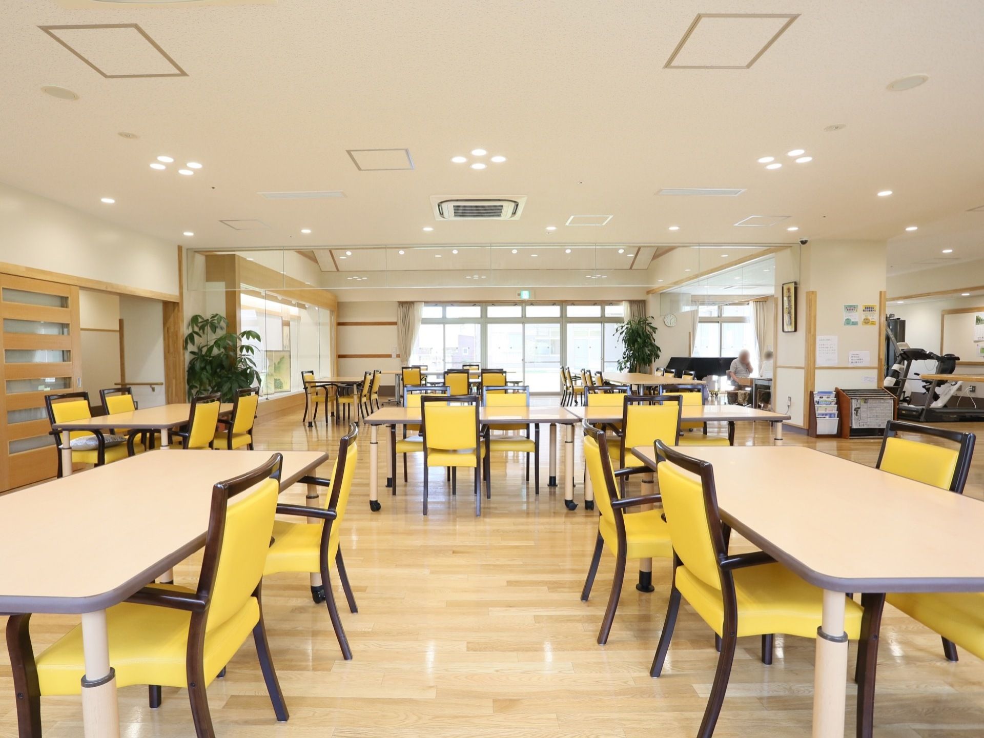 広く明るい部屋に、白いテーブルと黄色い椅子がゆったりと配置されている。部屋の隅には観葉植物が置かれマガジンラックもある。