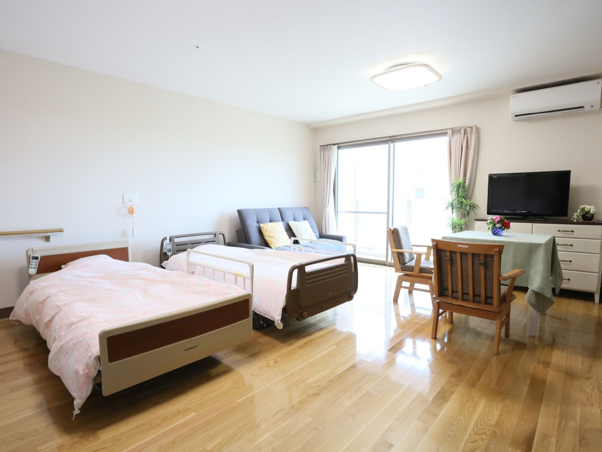大きな掃き出し窓があり明るく広い部屋にはリクライニングベッドが２台並んでいる。窓横に置かれたチェストの上にはテレビがある。