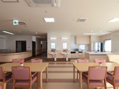 木目調のテーブルと肘掛けが付いた椅子が設置されている。奥にはキッチンと洗面台がある。天井には空調設備や、非常口の誘導灯が付いている。
