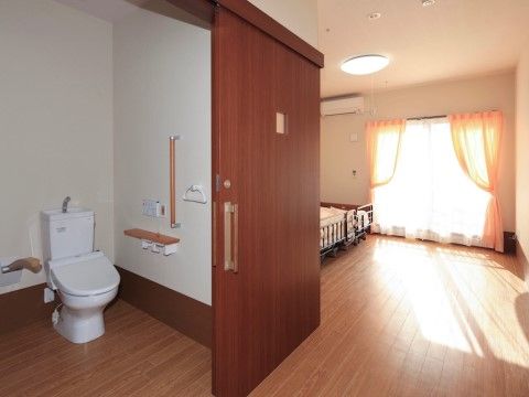 窓から光が降り注ぎ、明るいフローリングの居室になっている。トイレは温水洗浄便座が設置され、手すりも付いている。