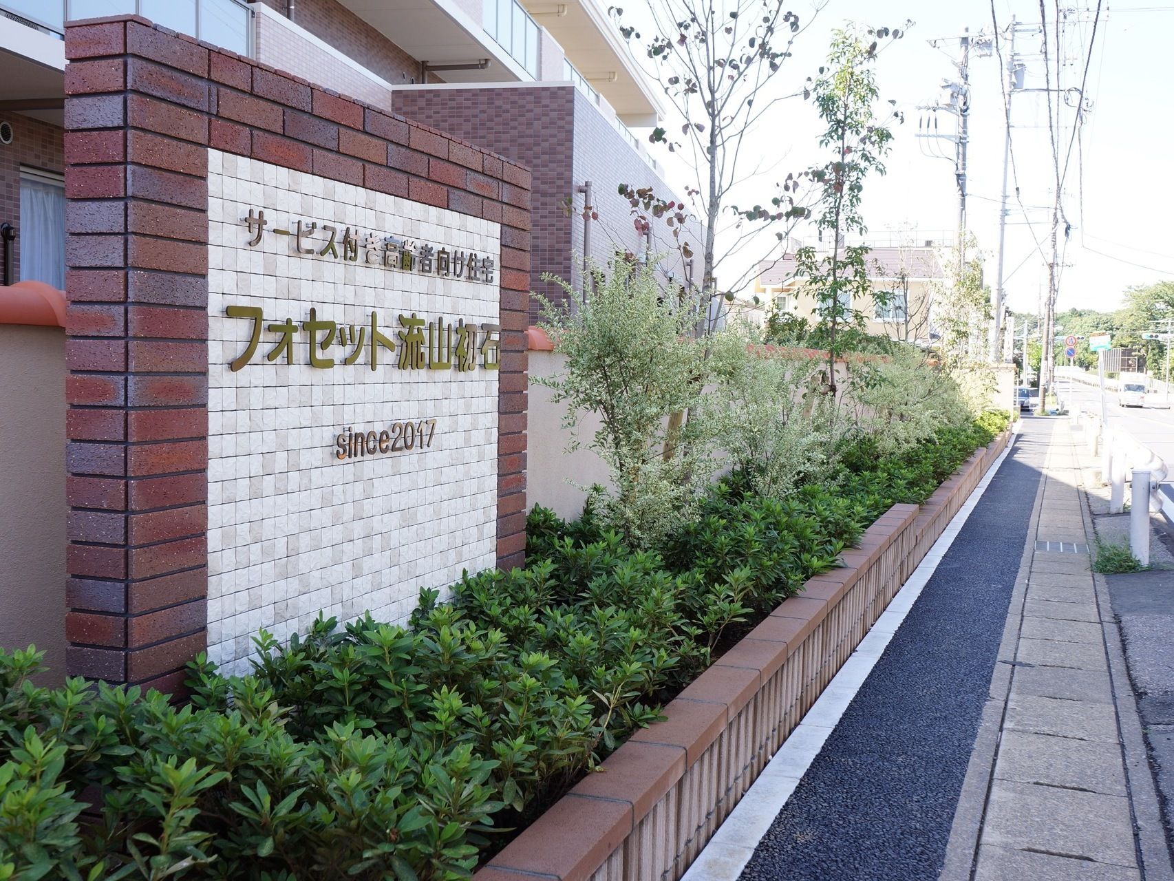 施設の敷地と道路との境には塀があり、プライバシーが守られている。外部には異なる高さの木々が多く植えられている。