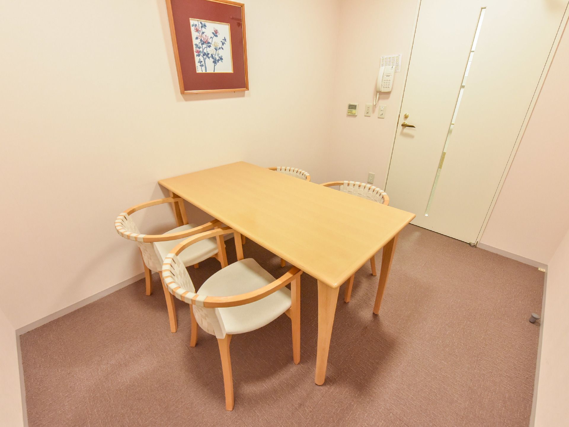 小さな部屋には長方形の机と白い背もたれの椅子だけがある。壁には花の絵の額と電話がある。ドアは内側に開く。