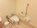 トイレの左右の壁には、ベージュ色の頑丈な手すりが付いている。ペーパーホルダーが2つあり、その上には緊急ボタンもある。