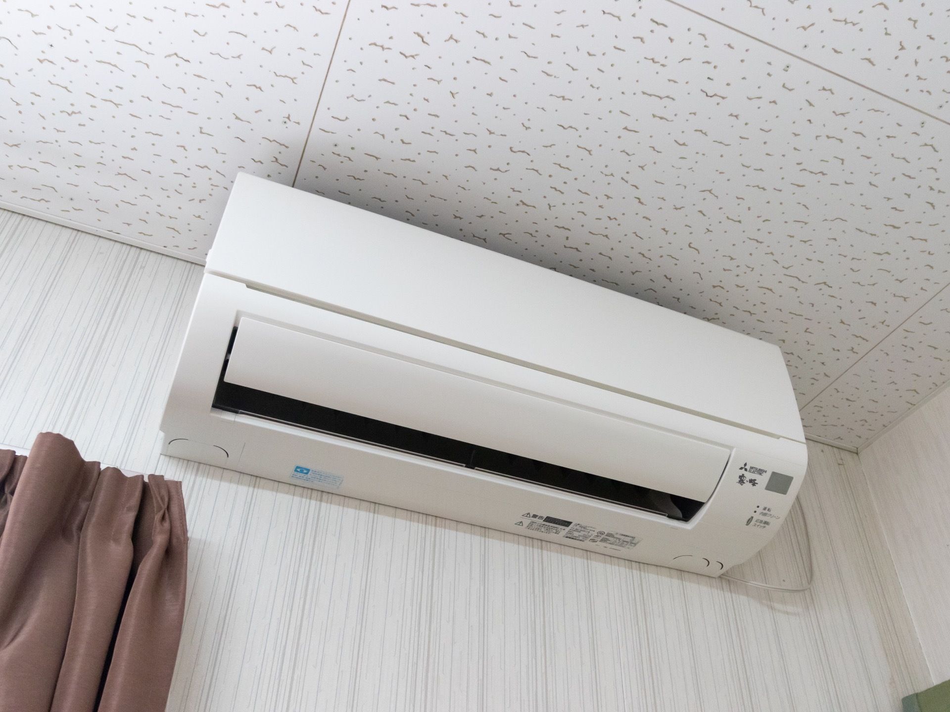 全面的に白く塗られた壁紙で、縦の線がうっすらと入ったデザインである。天井付近の隅には、エアコンが取り付けられている。