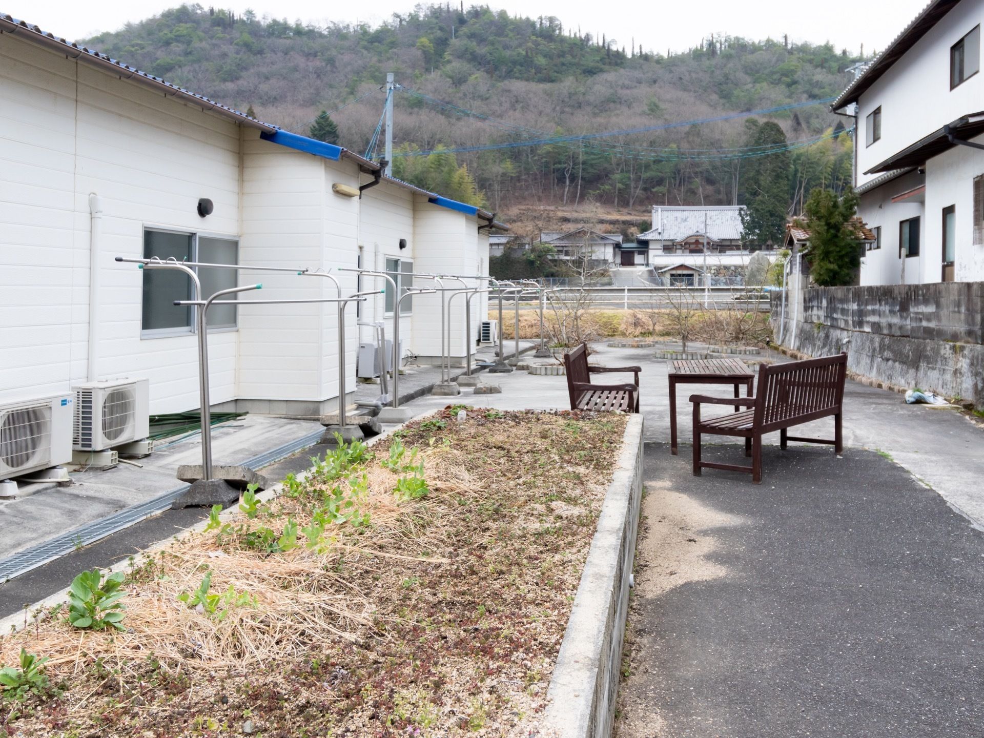 施設の裏側に、物干し台が4台設置されている。その側には、樹木が植えられ木製のテーブルやベンチが置いてある。