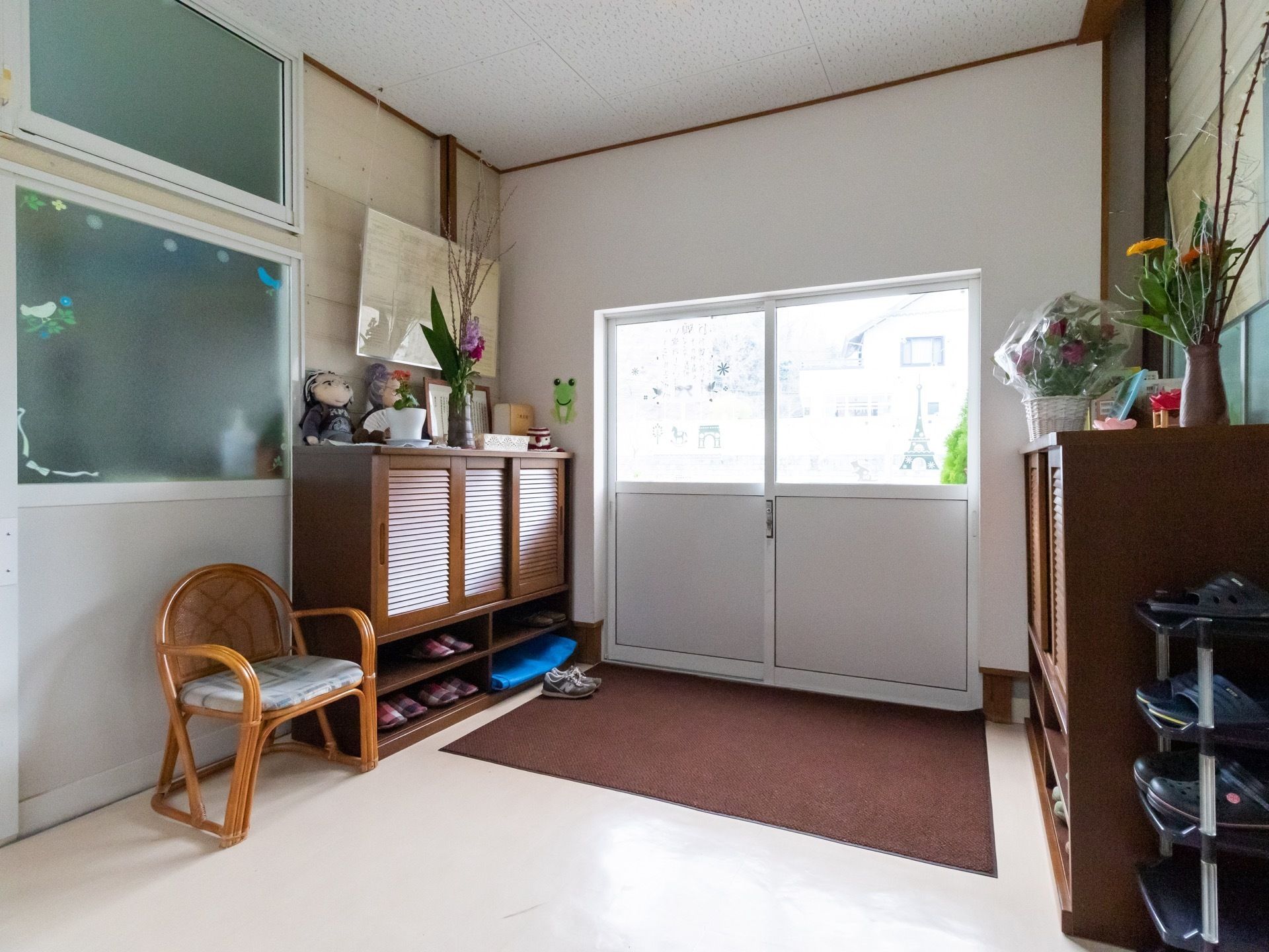 引き戸の玄関扉が中央にあり、床に茶色の玄関マットが敷かれている。両側の壁には下駄箱が備え付けられている。
