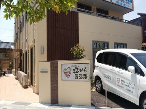 施設名が書かれた親しみやすい看板のある施設入口と専用の車