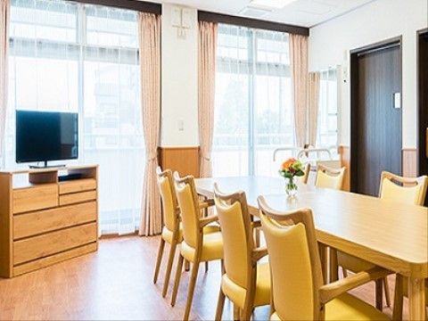 木製のテーブルと椅子、テレビが設置されている。食堂全体に陽射しがよく入り、白い壁も相まって明るい雰囲気の部屋である。