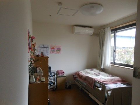 横側に大きな窓があり明るい空間の居室である。傍に介護用ベッドを配置し、天井下にエアコンを完備している。愛用の家財道具を備えている。