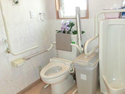 隣に男性専用の便器も備えたトイレスペースである。窓から日の光が射し込み明るい空間である。便座傍や壁に手すりを完備している。