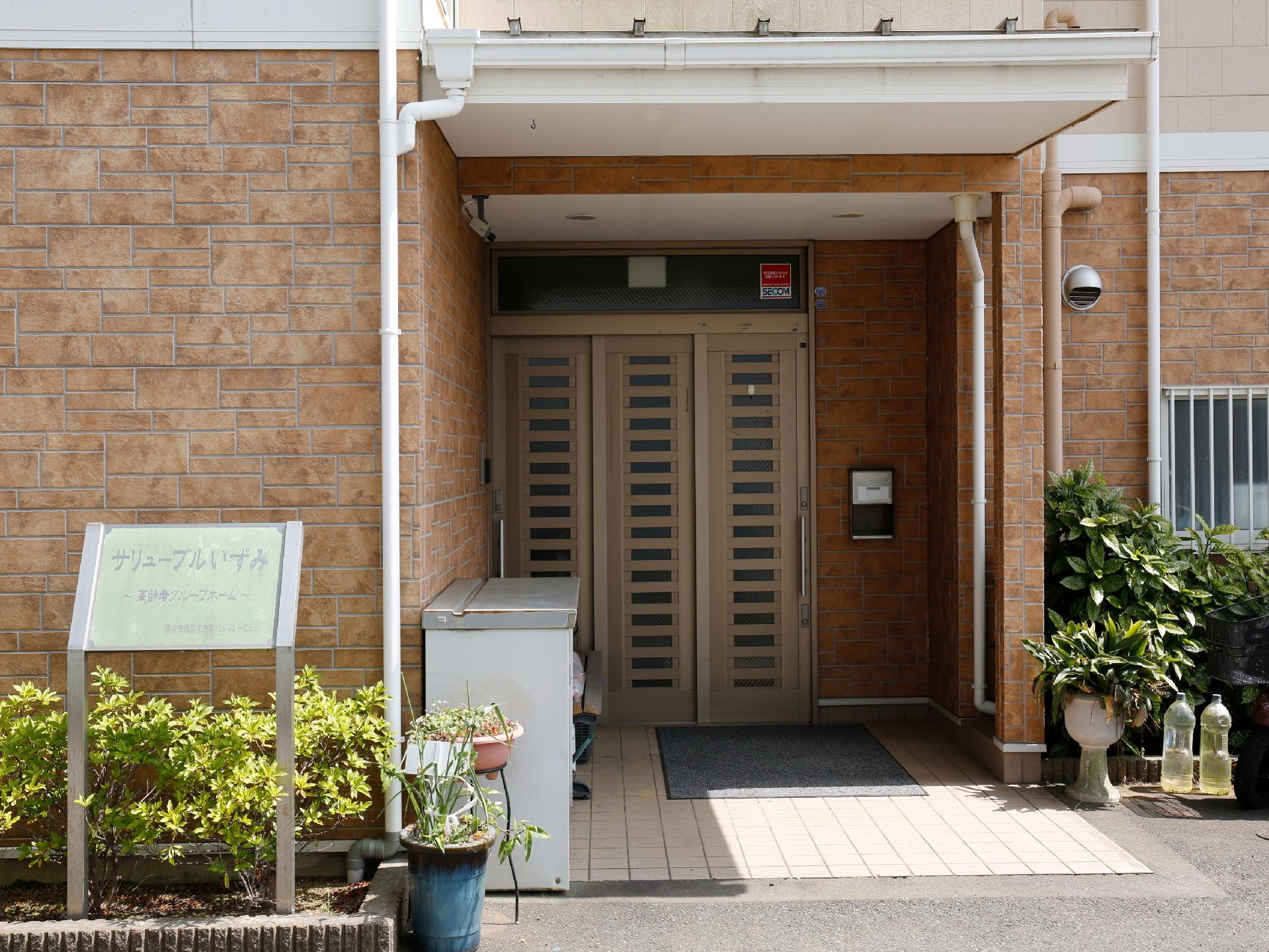 看板のすぐ横が玄関になっている。扉は、スライド式で開け閉めしやすい構造。扉の前には郵便受けが設置されている。