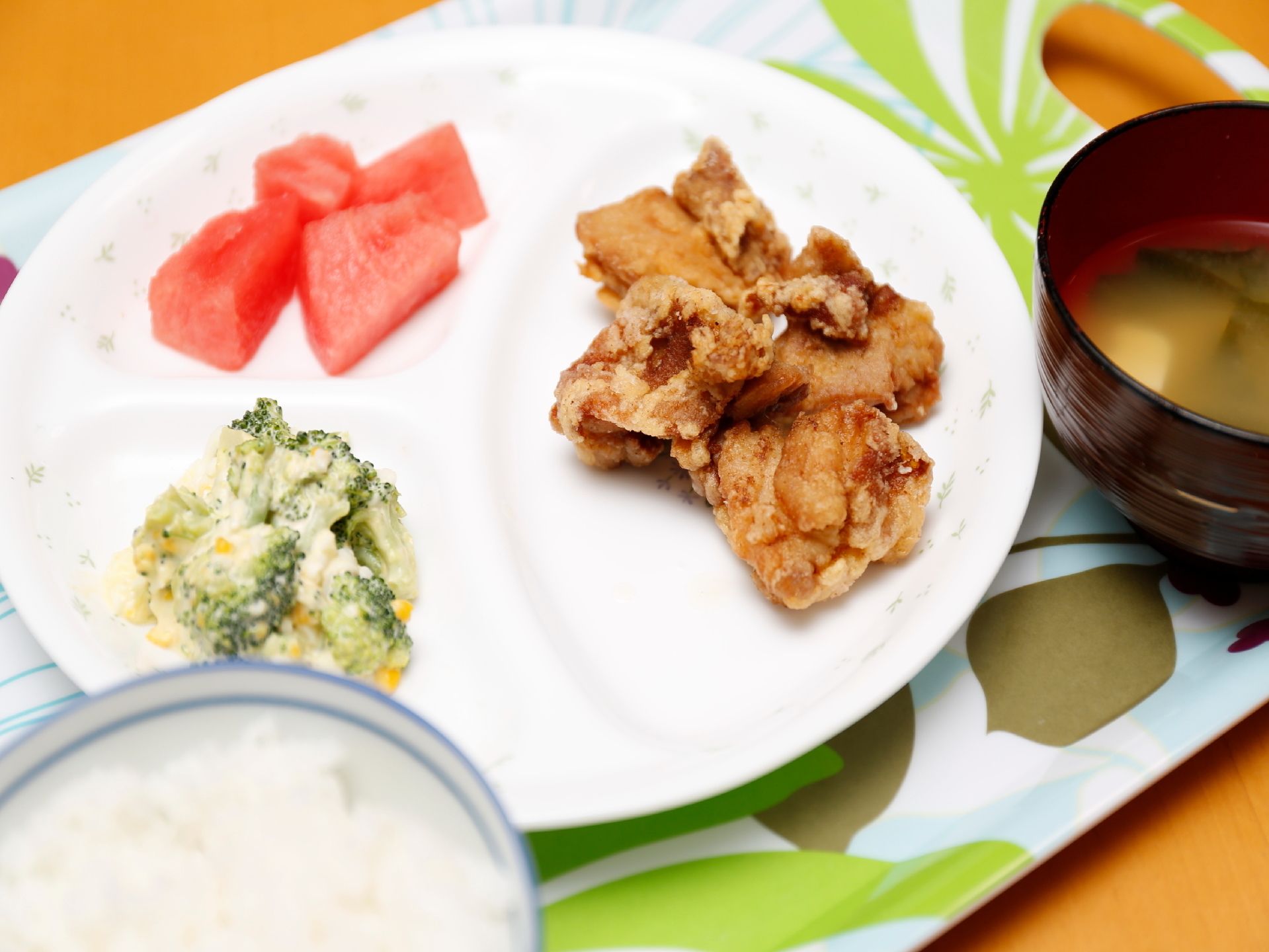 施設内での食事の一例。写真は唐揚げ、ブロッコリーの和え物、ご飯、お味噌汁、スイカである。栄養バランスをきちんと考えられている。