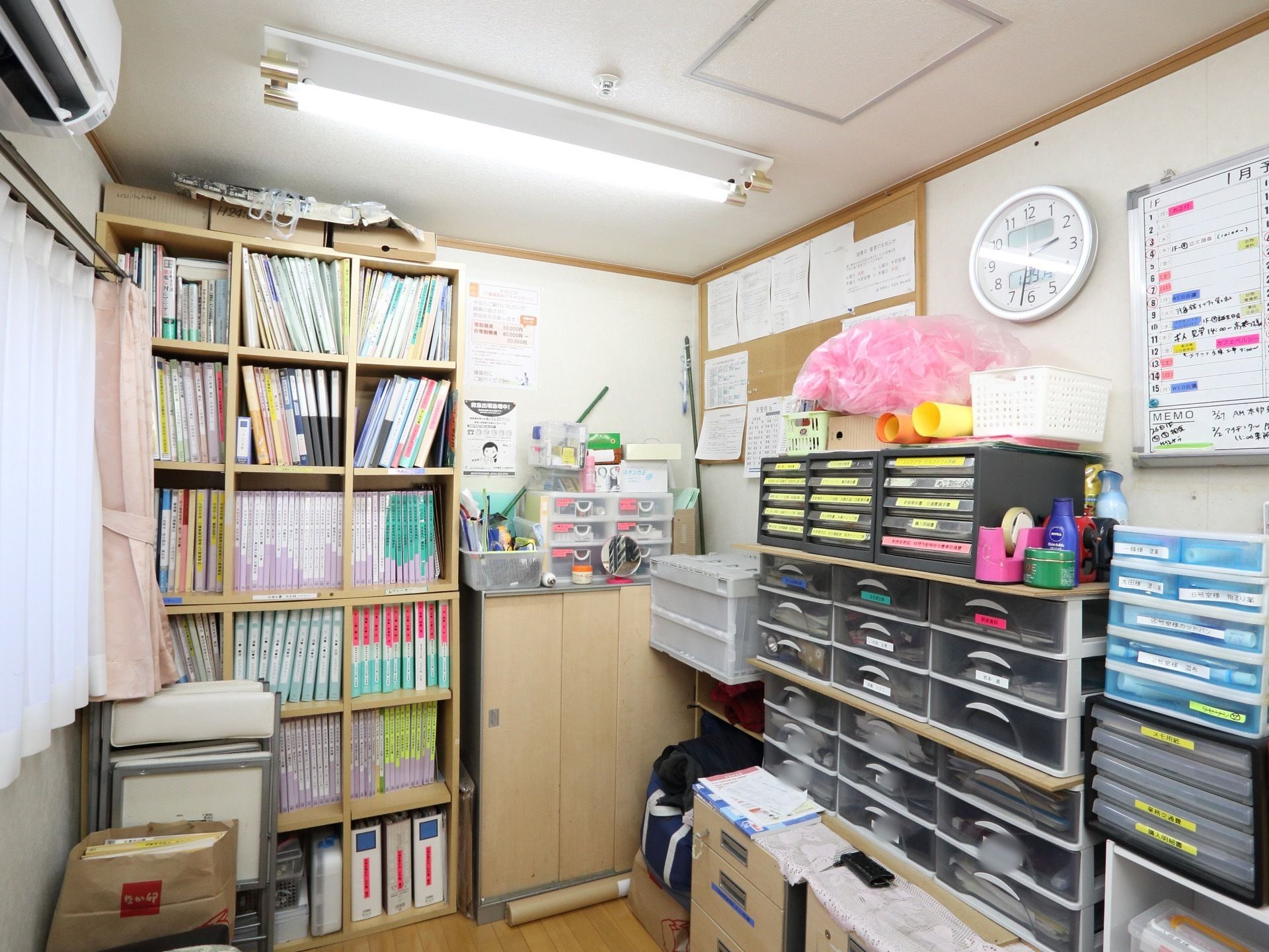 整理整頓されたスタッフルーム。多くの書類が分類分けされて本棚や書類箱の中に収まっている。日程表も設置している。