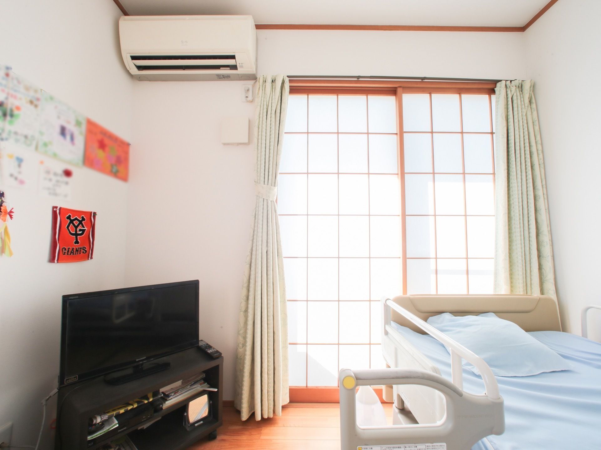 居室に空調と電動ベッドを設置している。窓から障子越しに明るい陽が入る。カーテンがあるため、部屋の明るさを調節できる。