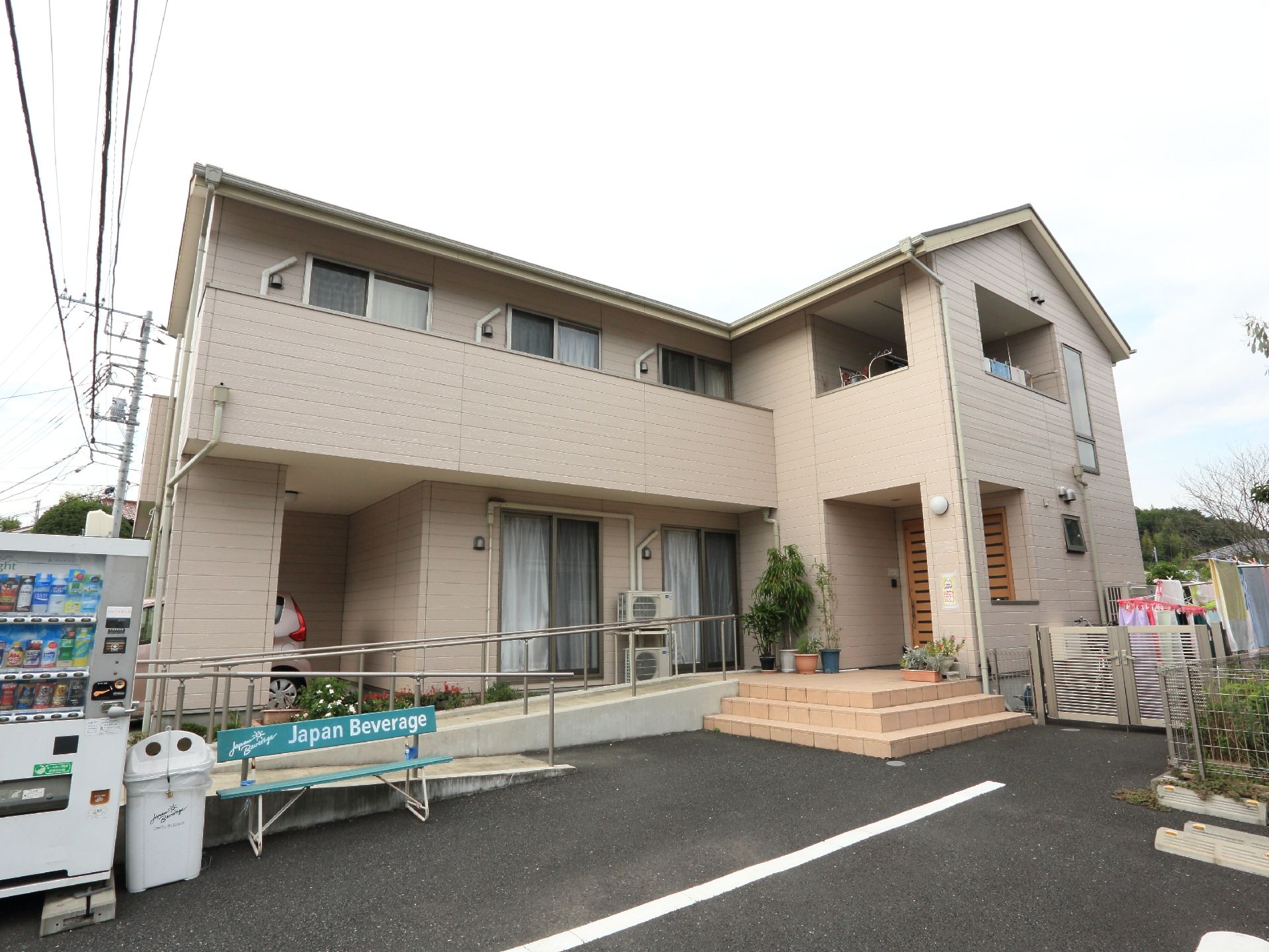 外観の前にベンチと自動販売機がある。玄関前は階段のほかになだらかなスロープがついていて、手すりが設けてある。