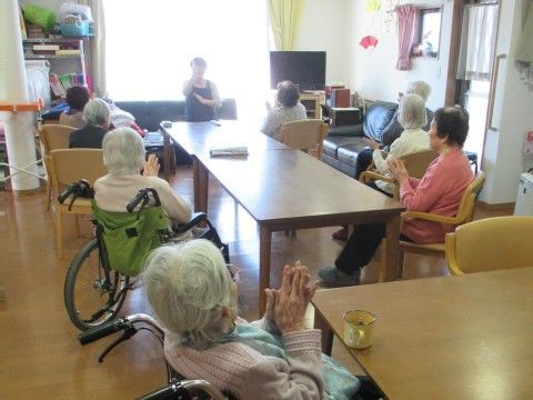 ダイニングテーブルを縦につなげてレクリエーションを行っている。スタッフの女性に合わせて入居者様が手を動かしている。
