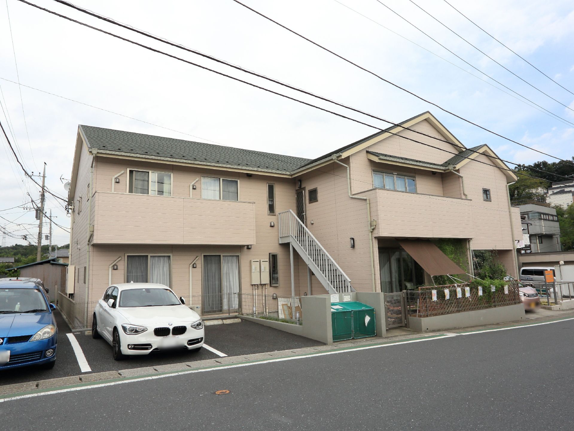 緑が多い住宅地に建てられている2階建ての施設の外観。敷地内にコンクリートで整備された駐車スペースが設けられている。