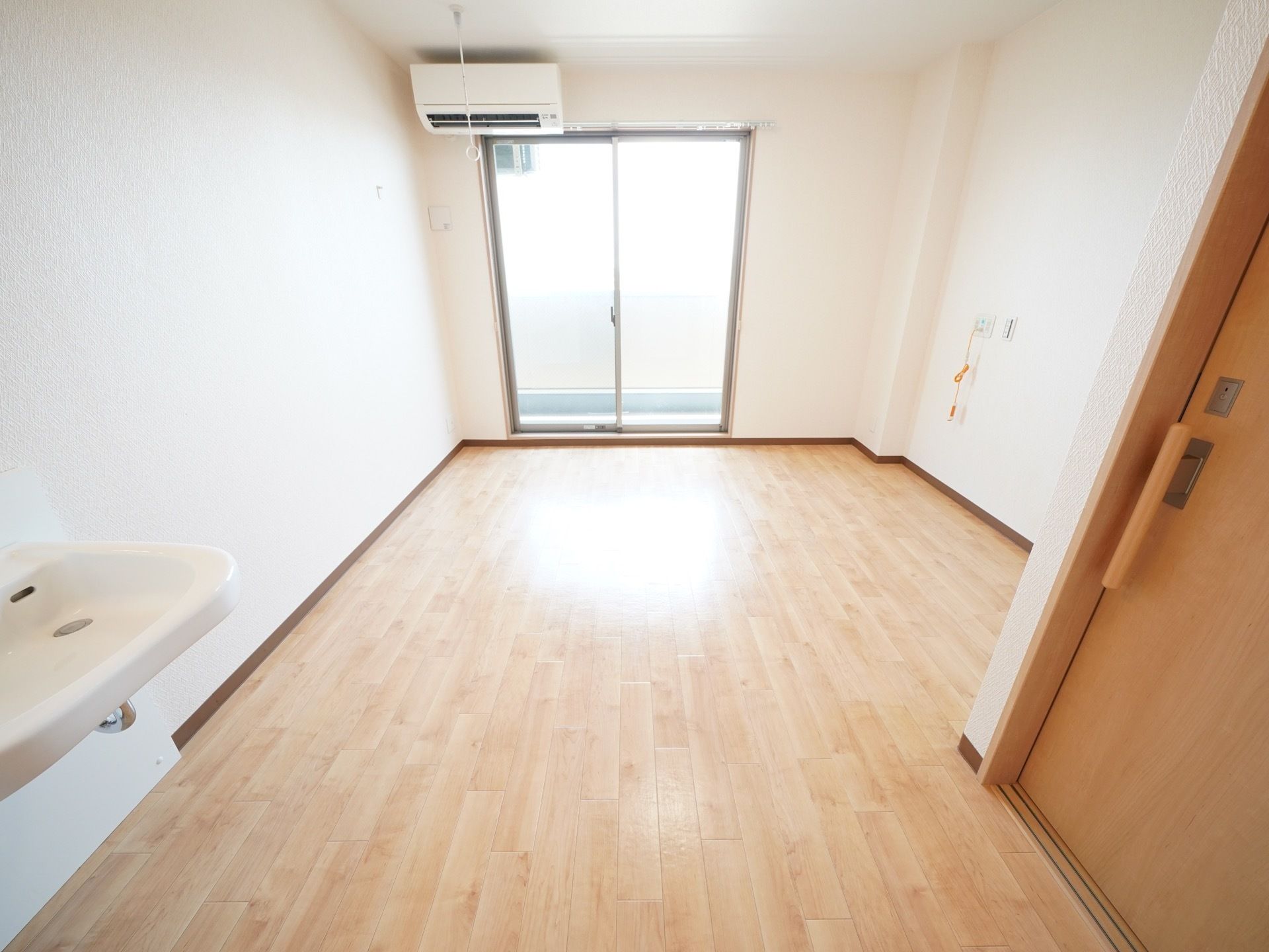 ベランダに出ることができる大きな窓が設置されており、明るい日差しが差し込んでいる。右側の壁にナースコールが取りつけられている。