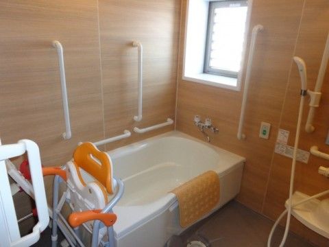 窓がある明るい浴室。シャワーは高さが変えられる。浴槽周りには手すりが複数あり、折り畳み式のシャワーチェアがある。