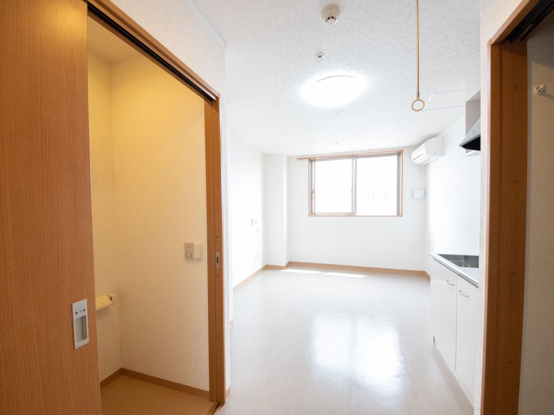 居室は、正面に窓があり明るい空間である。横側の壁際にエアコンを設置している。トイレの出入口は広々とし、木目調の引き戸を取り入れている。