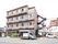 道路に面した住宅街に位置する４階建ての建物である。居室の窓が並び、ベランダには、格子のフェンスを設置している。横側に非常階段を設けている。