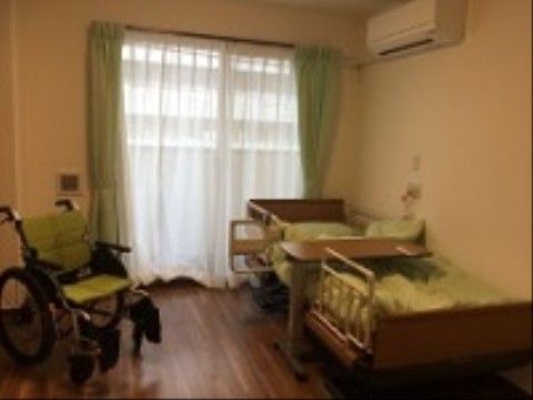 エアコンが完備されたワンルームの居室である。転落防止のための柵が付いた介護ベッドと車椅子が置かれている。