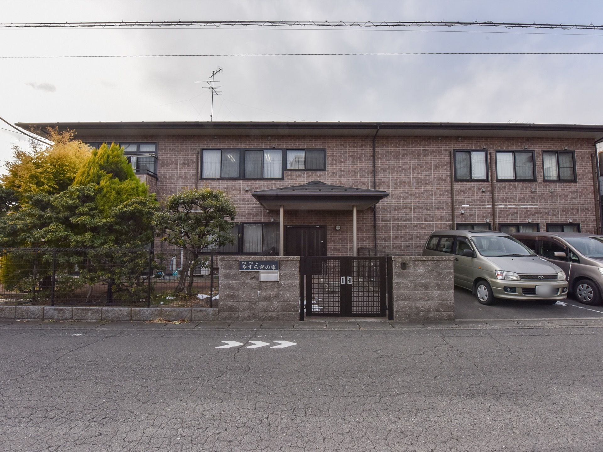 生活道路に面する２階建ての施設。塀に施設の看板を取り付けている。敷地に柵と門を設置しているため、不審者の侵入を防ぐことができる。