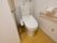 洋式便器が設置されている。壁側には手すりがあり、その上にはトイレットペーパーフォルダー、下には呼び出しボタンがある。