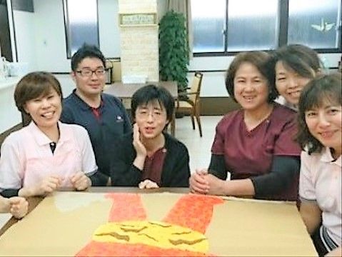 出来上がった工作の作品を前に並んで写真に納まる施設のスタッフ