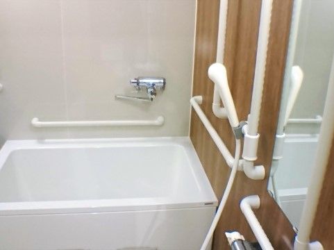 ひとり用サイズのバスルームに、浴槽、ミラー、シャワーなどが取り付けてある。シャワー周辺や浴槽周りには手すりが付けられている。