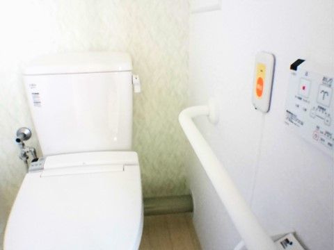 温水洗浄便座を設置している。壁面に操作パネルがある。手すりや呼出ボタンを取り付けて安全に配慮している。