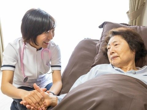 居室内で、入居者様の手を握り、笑顔で話しかけるスタッフの様子
