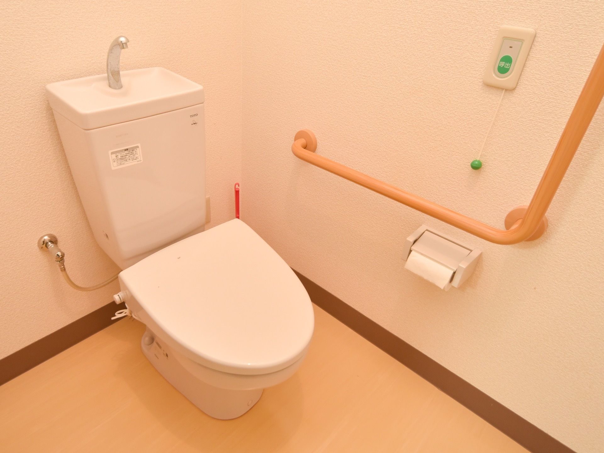 トイレには暖房便座のついた洋式便器を設置している。また床には掃除道具があり、壁にはナースコールを備え付けている。