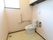 開放的な洗浄便座付きのトイレである。棚にはトイレ用品などが収納されている。壁には手すりやペーパーホルダーが取りつけられている。