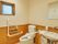白を基調に木目を取入れたトイレスペースである。便座と洗面台を並べて備えている。壁にエル型の手すりを設け、その上に小さめの窓がある。