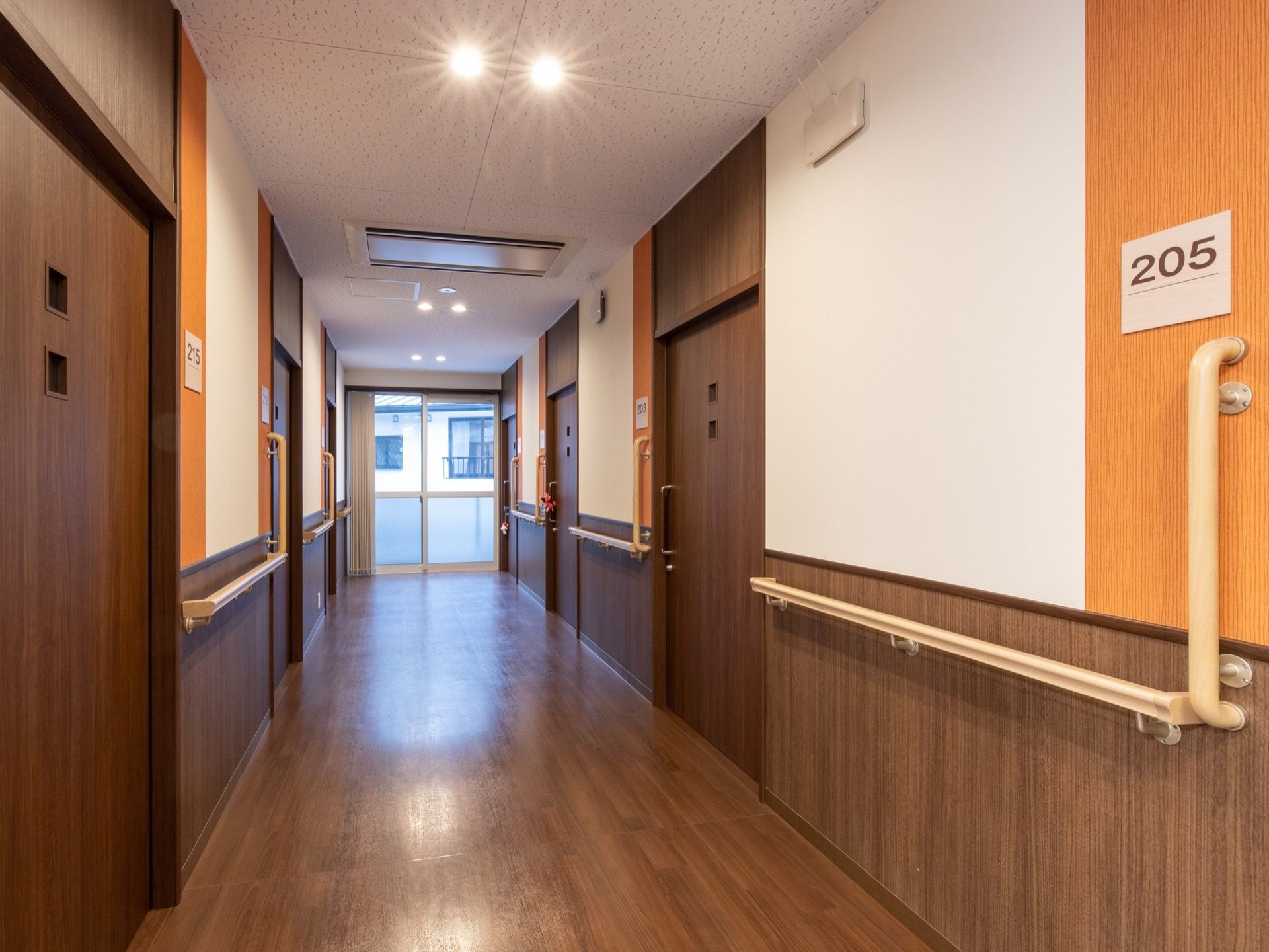 通路は、ダークブラウンを基調とした建具が使われ、シックな雰囲気である。照明が暖色系で目に優しい。部屋番号の表示が大きく見やすい。