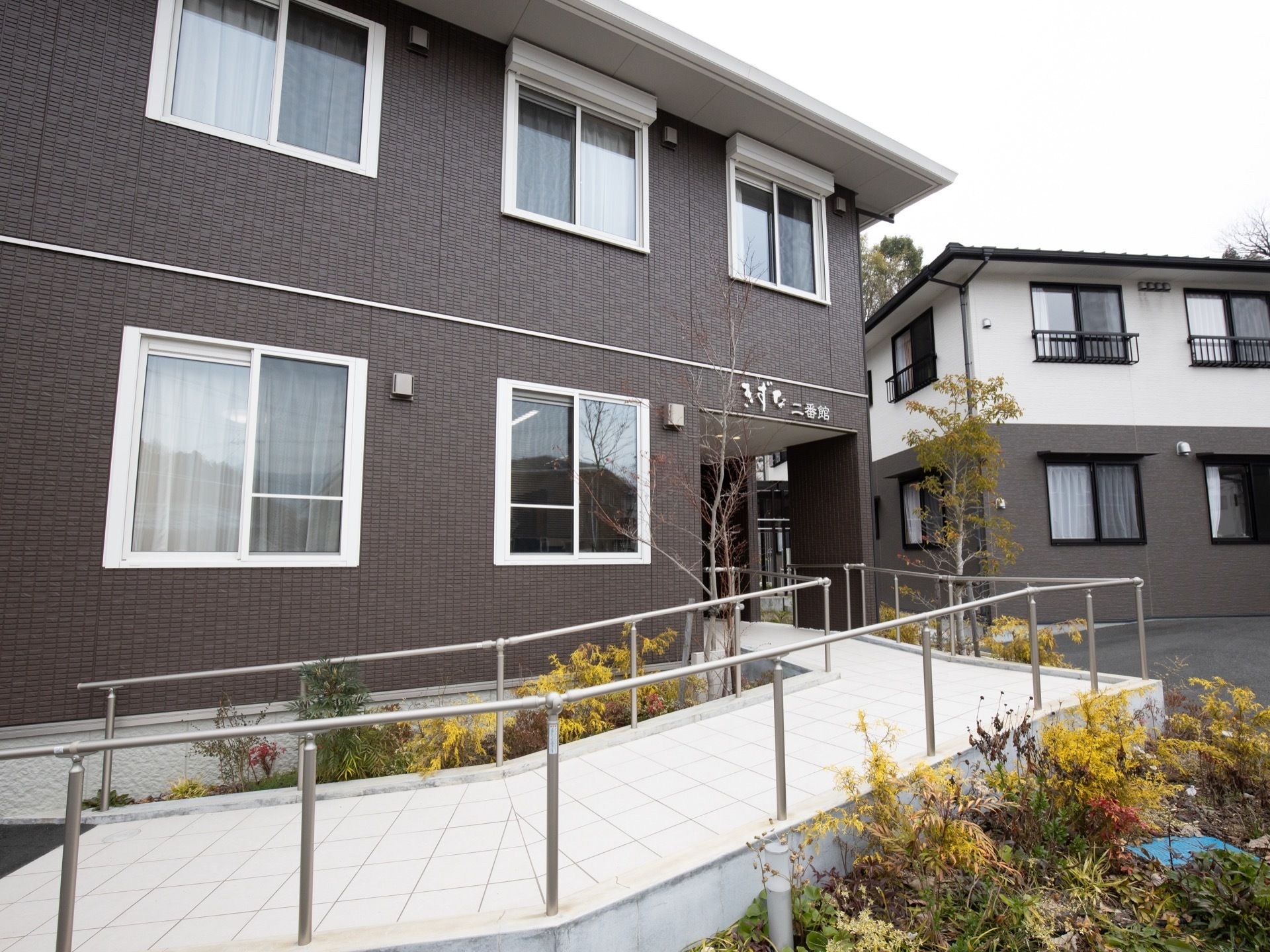 敷地から玄関への道のりは手すりのついたスロープとなっている。緩やかな傾斜で、誰でも出入りしやすいような造りである。