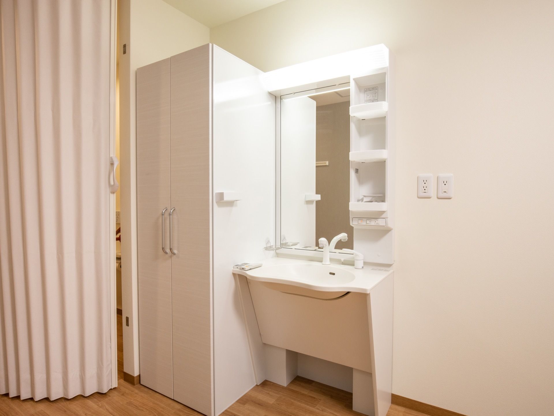 居室に洗面台が備えつけられている。真っ白で清潔感があり、明るい照明である。収納ポケットも豊富で、洗面用具を入れておくことができる。
