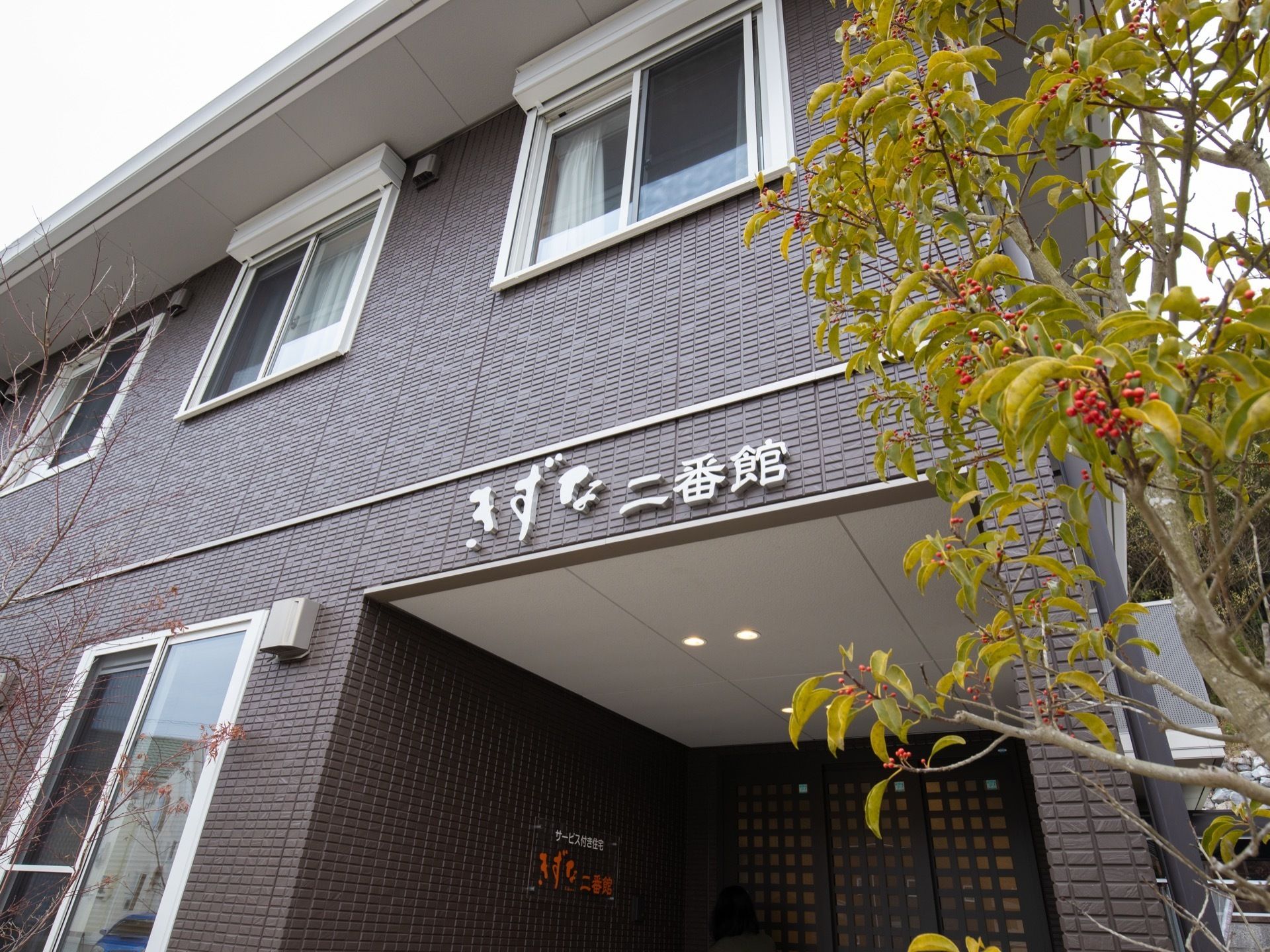 ダークグレーの外壁に、入口の頭上には施設名のプレートが取りつけられている。スタイリッシュな見た目の外観となっている。