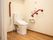 居室にはトイレが備えつけられている。壁には斜めに固定された手すり、可動式の手すりが左右に取りつけられている。